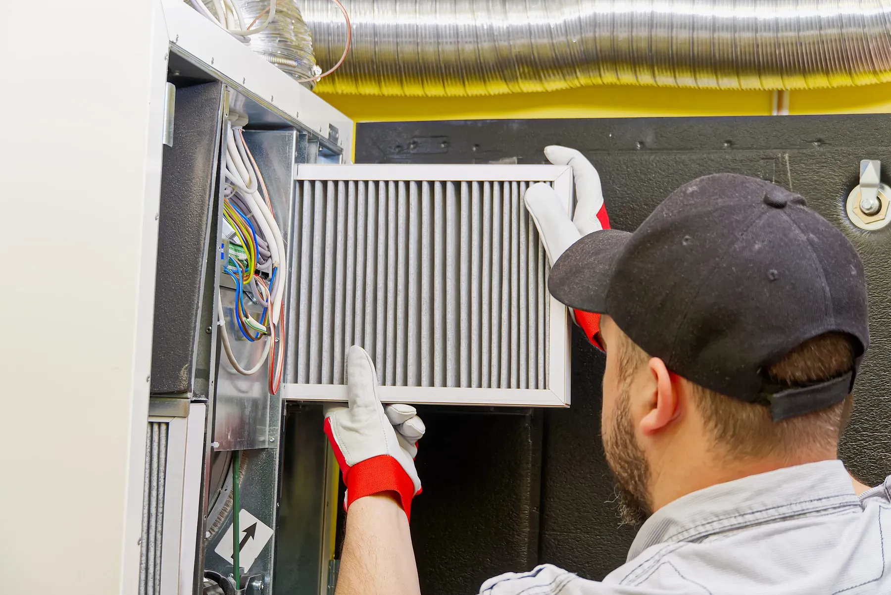 Homeowner sliding a fresh pleated air filter into a return-air grille