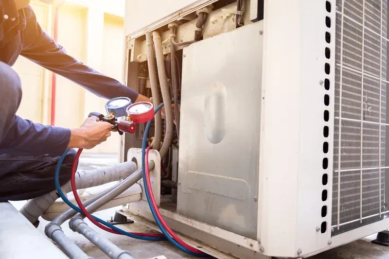 HVAC technician crouched beside an outdoor condenser unit, checking its condition