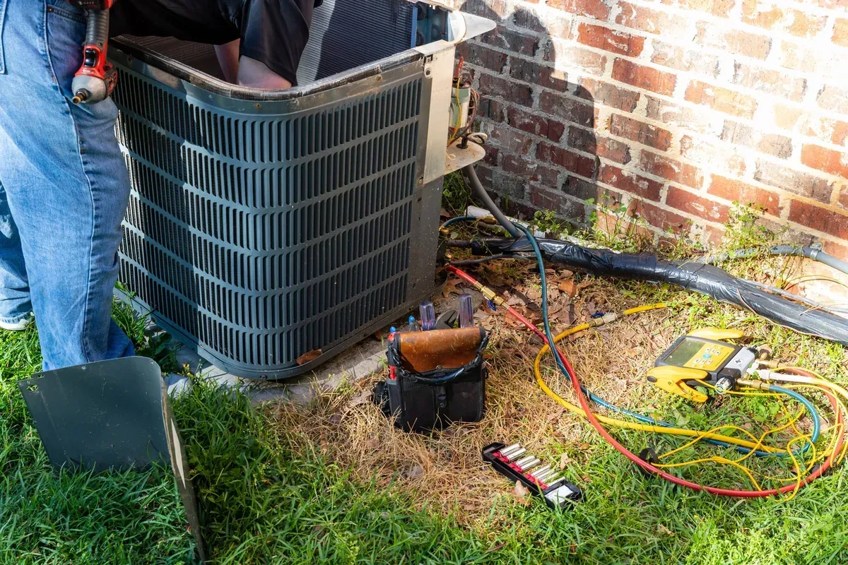 Outdoor air conditioning condenser unit installed against a brick exterior wall of a single-family home